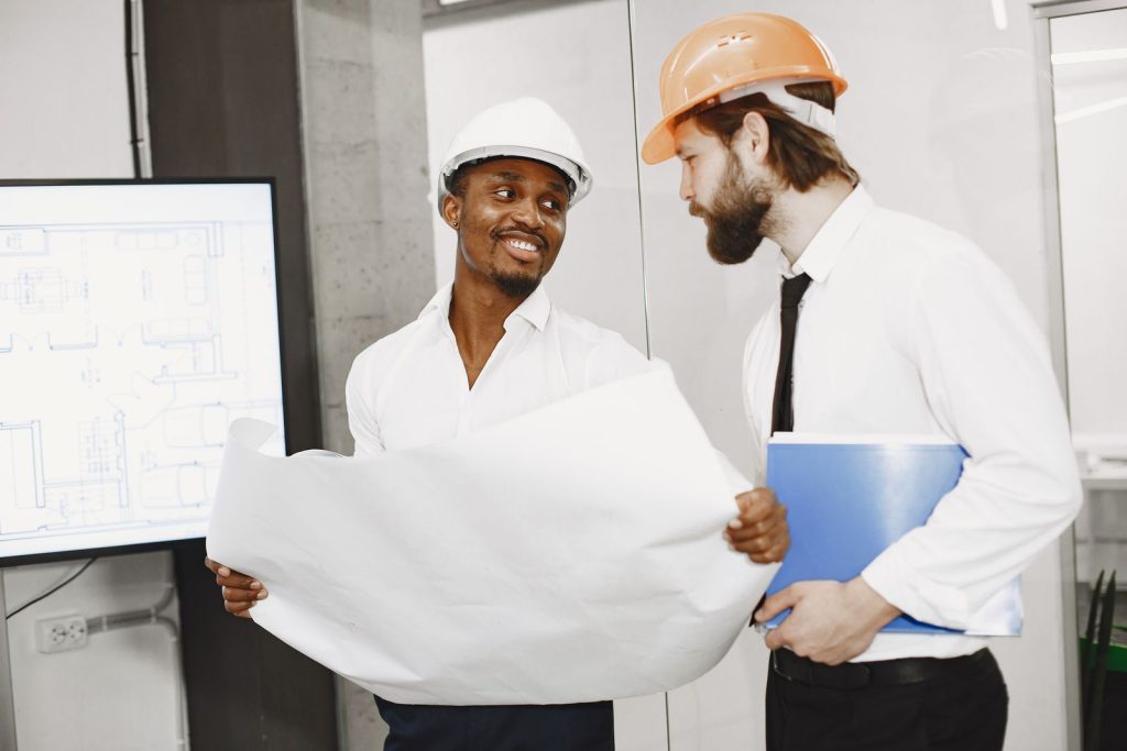 Two project leads in hard hats reviewing plumbing rough-in drawings
